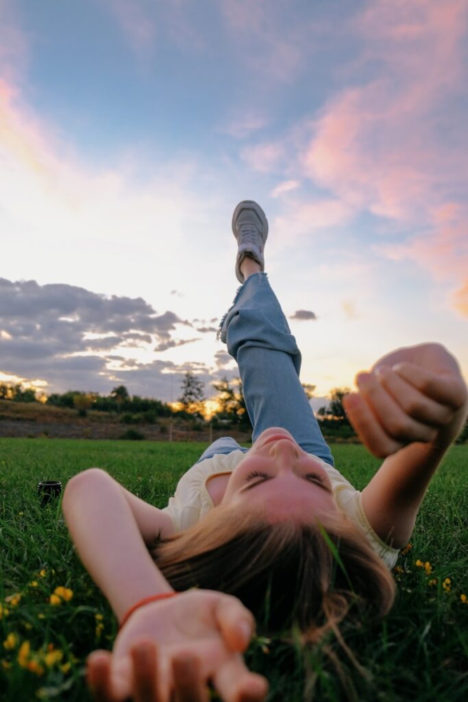 woman in white tank top lying on green grass field during daytime